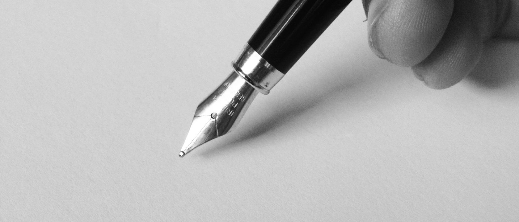 A fountain pen poised over a blank page, in black and white